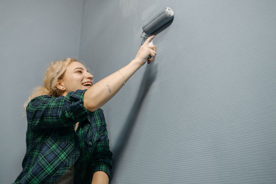 Mur en cours de peinture avec rouleau, pinceau, ruban de masquage et pot de peinture dans une pièce claire